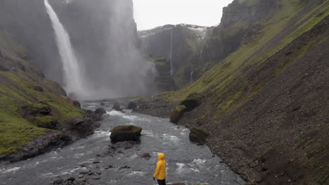 retroceso de drones para revelar a una persona de pie sobre una roca, cerca de la cascada de haifoss en islandia