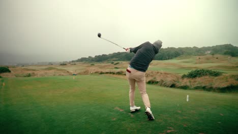 male golfer hits golf ball with driver off tee on tee box on foggy day on ireland links golf course in slow motion