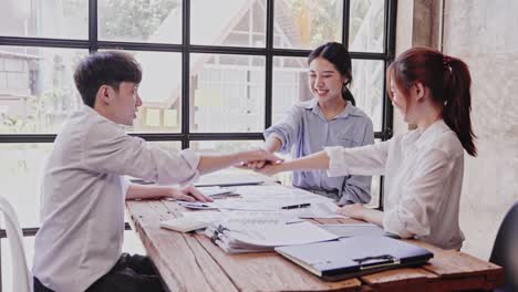 fashionable young asians excitedly stack their hands in smart casual outfits while working in a creative office. the concept was successful.