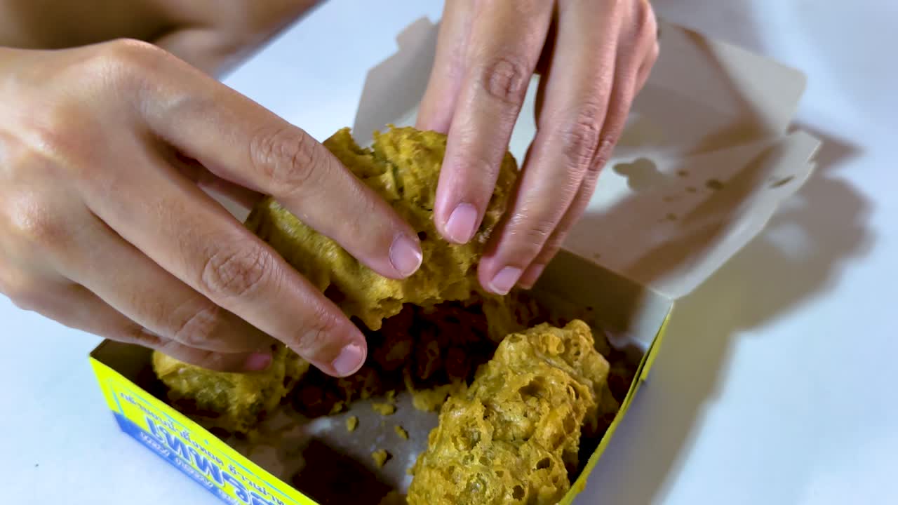 las manos interactúan con bocadillos fritos, revelando un relleno verde vibrante, en un entorno bien iluminado, mostrando comida callejera tailandesa