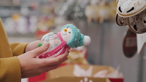 el comprador tiene un muñeco de nieve de juguete en sus manos - elige adornos para el árbol de navidad