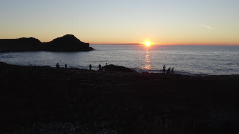 Stunning sunset over the sea horizon at Giants Causeway with shilouetted tourists. Aerial pan