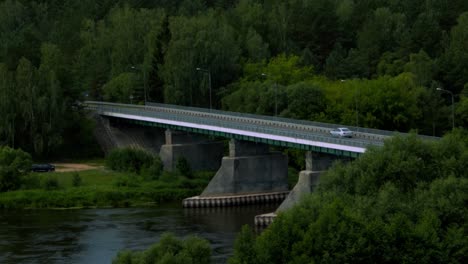 moody shot of car driving on a bridge with green forest around it