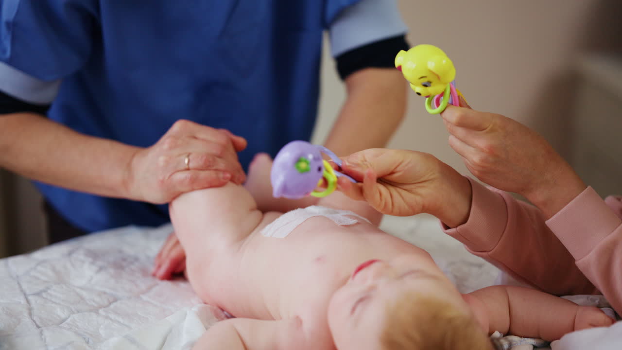 Donna che cerca di distrarre un bambino che piange, sdraiato su una coperta durante un massaggio, con un giocattolo.
