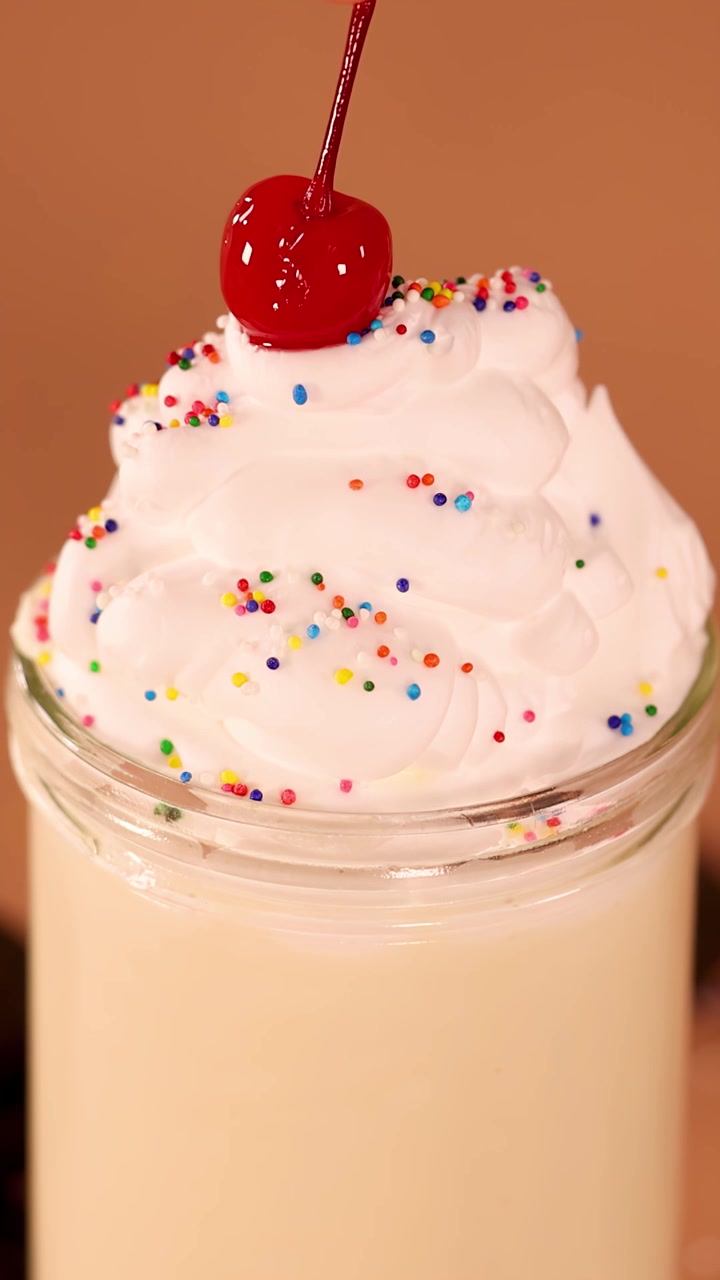 Primo piano di milkshake alla vaniglia mentre una ciliegia al maraschino si posa delicatamente sulla panna montata con codette