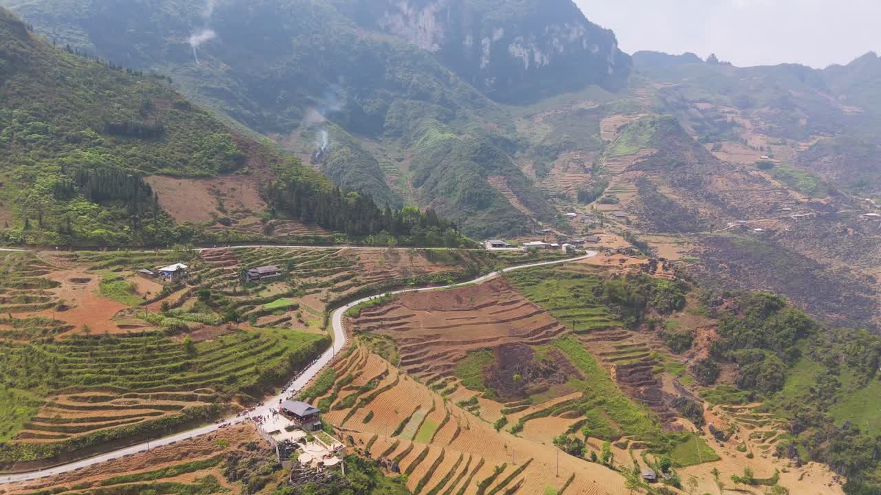 A scenic aerial view of Ha Giang's serpentine roads, highlighting motorcycles riding through vibrant green rice fields surrounded by majestic mountains.