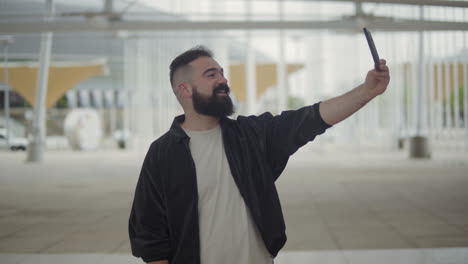 hombre barbudo sonriente haciendo una videollamada a través de un teléfono inteligente.