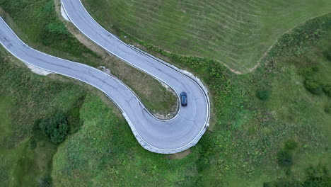 Coche-Tomando-Una-Curva-Cerrada-En-Un-Bosque-Cubierto-De-Hierba-Vista-Aérea-De-Arriba-Hacia-Abajo-De-La-Carretera-De-Montaña