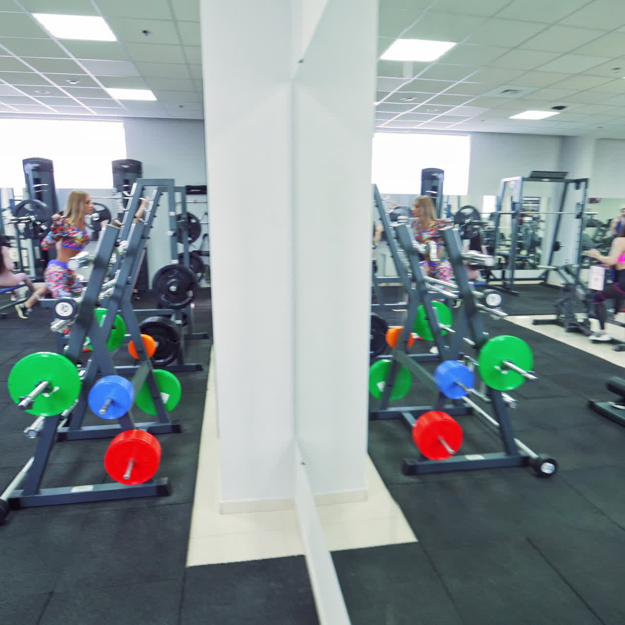 Young sportswomen in fitness clothes training in a modern gym. Sports center with beautiful girls working with dumbbells, barbells and exercising on simulators