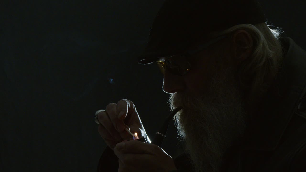 Cool mature man silhouette with beard lights pipe: Dark room portrait