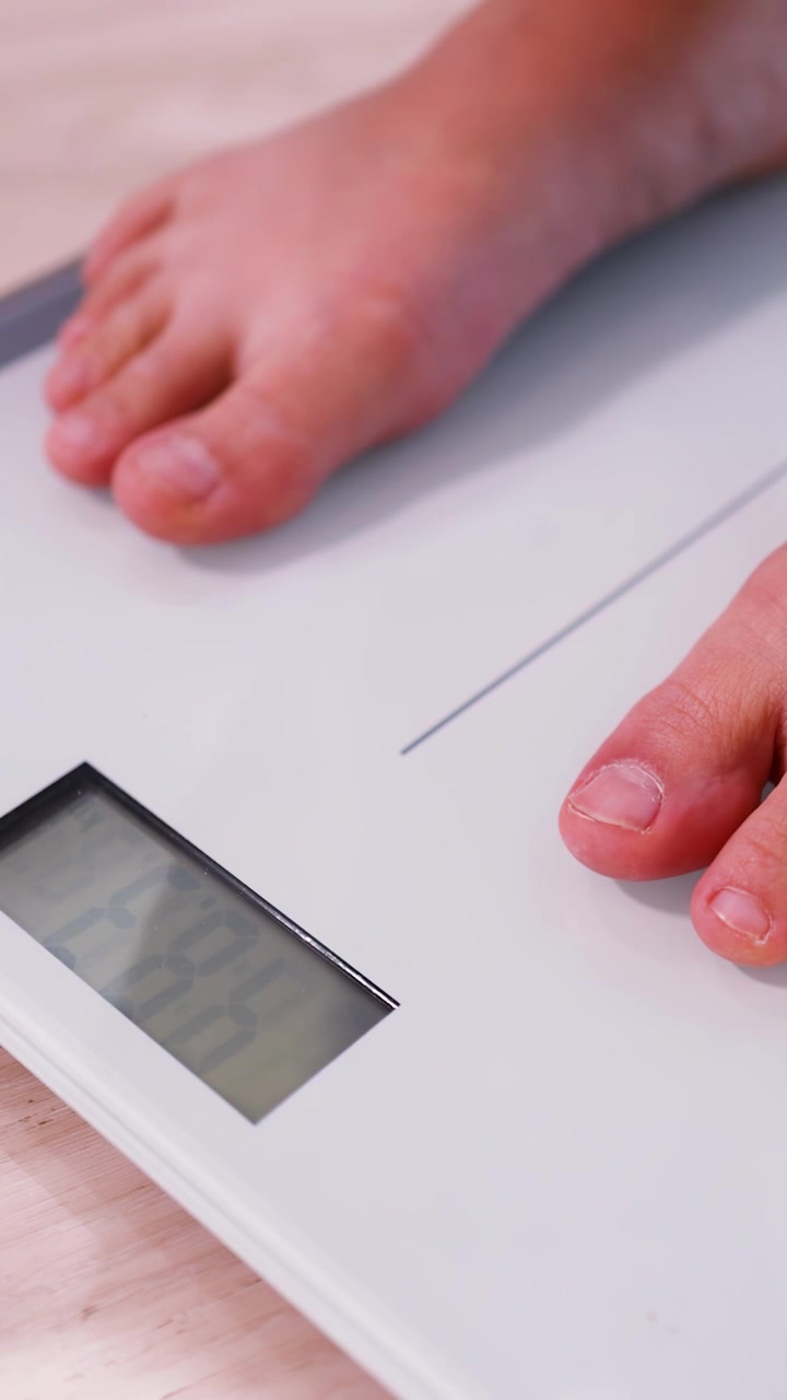 Bare feet step onto a white digital scale showing a weight of 48.3 kilograms