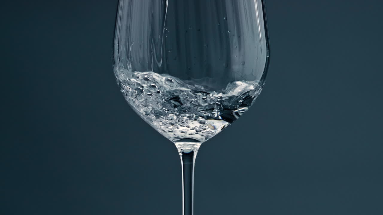 Close-up de água límpida a encher um copo. Bebida pura e refrescante a ser vertida num copo transparente.