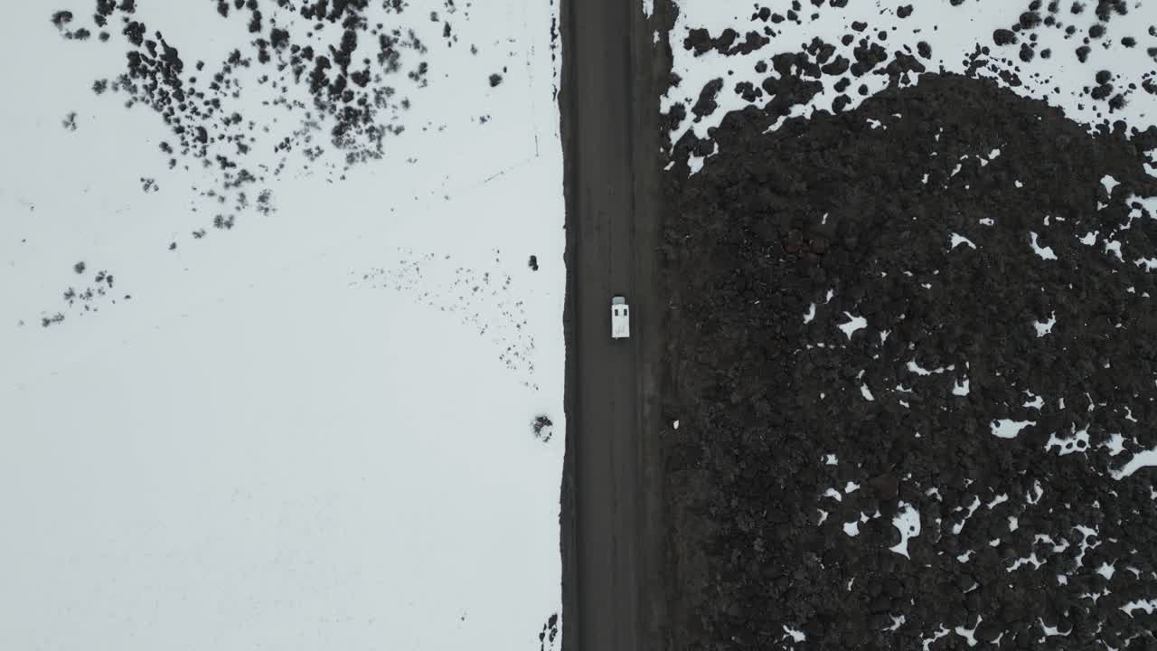 공중 전망은 아이다호의 눈 인 황량한 풍경을 여행하는 색 캠핑 밴을 포착합니다. 광활한 자연의 한가운데 여행, 모험, 밴 라이프의 정신을 구현합니다.