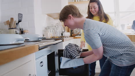 young downs syndrome couple taking homemade cupcakes out of oven in kitchen at home