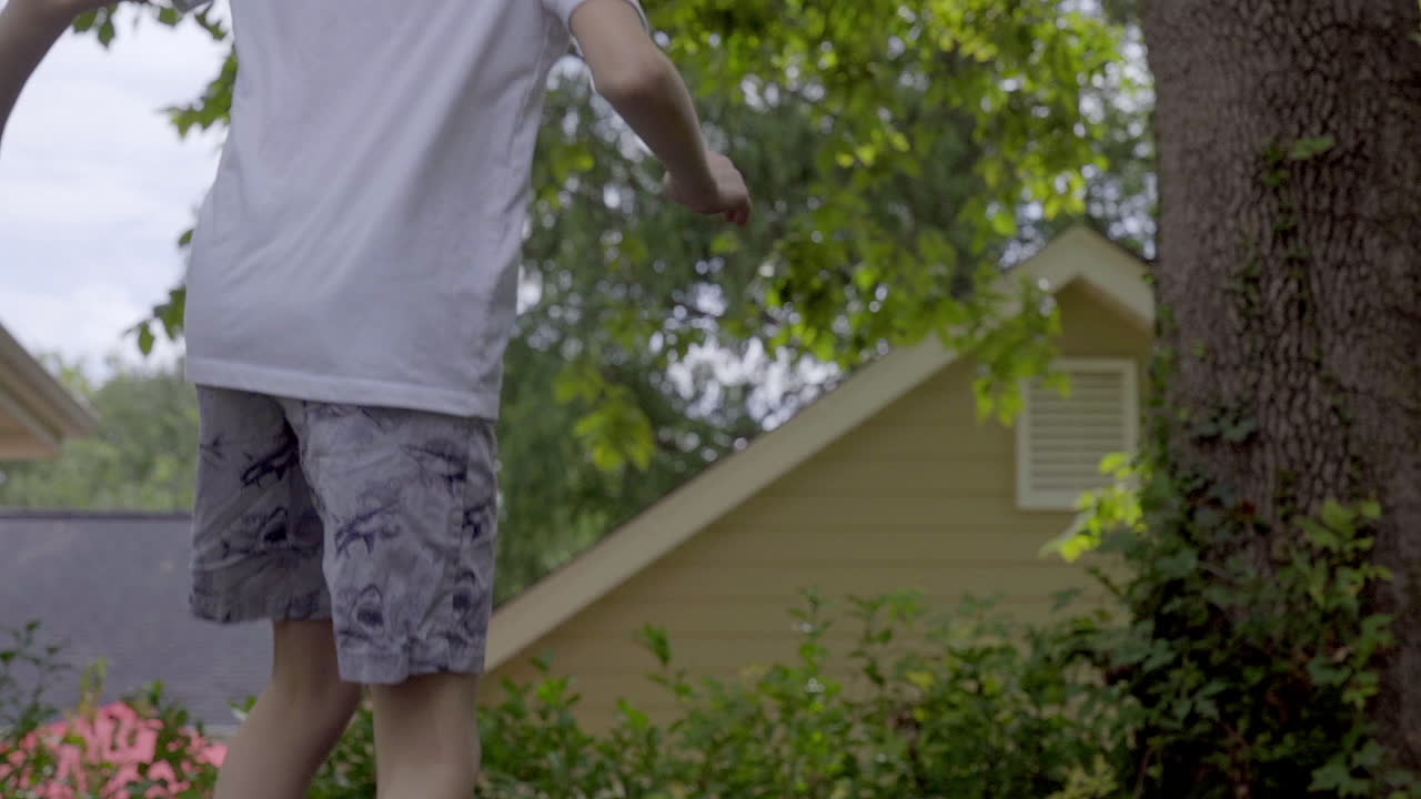 A cute boy jumps around on a trampoline in the backyard, medium shot slow motion