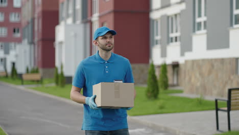 Der-Blaue-Zusteller-Schickt-Dem-Kunden-Ein-Paket,-Bevor-Er-Die-Fracht-Ausliefert.-4K-Auflösung-Und-Zeitlupenaufnahme.-Männlicher-Postbote-Mit-Paket-In-Der-Hand-An-Der-Stadtstraße.-Postkonzept.-Lieferservice.