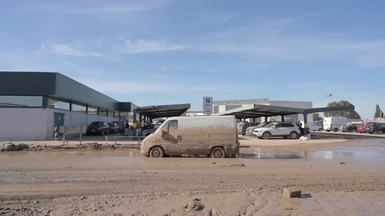 A van covered in mud is parked in a muddy parking lot after the DANA storm in Valencia