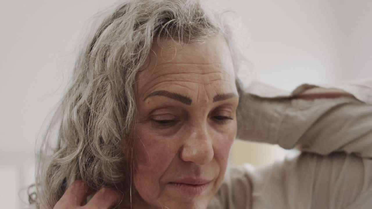 Donna anziana caucasica che sistema i suoi lunghi capelli grigi in camera da letto, al rallentatore.