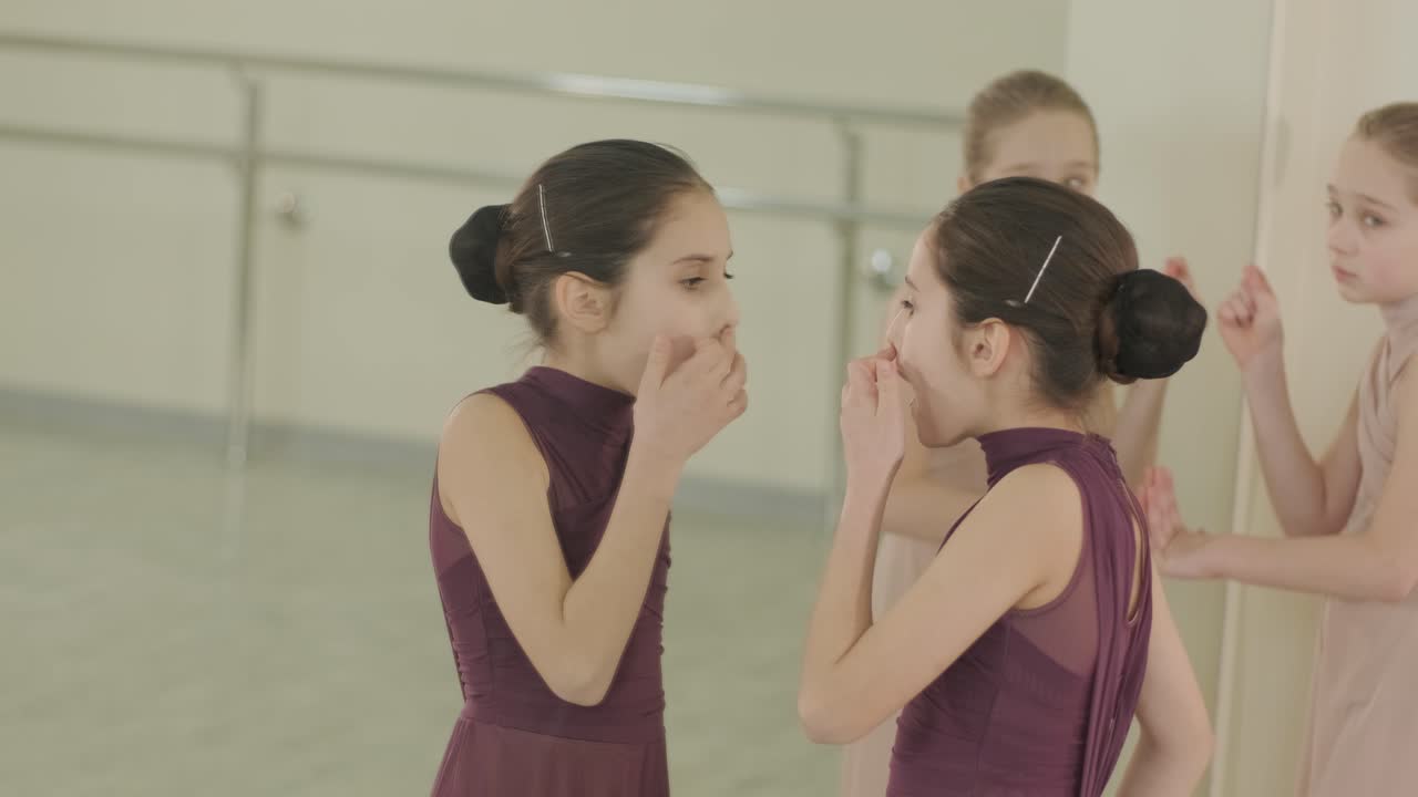 검은색 댄스웨어를 입은 젊은 발레 학생들이 나무 바닥과 벽에 장착된 바를 가진 넓은 발레 스튜디오에서 자세를 연습하는 그룹.