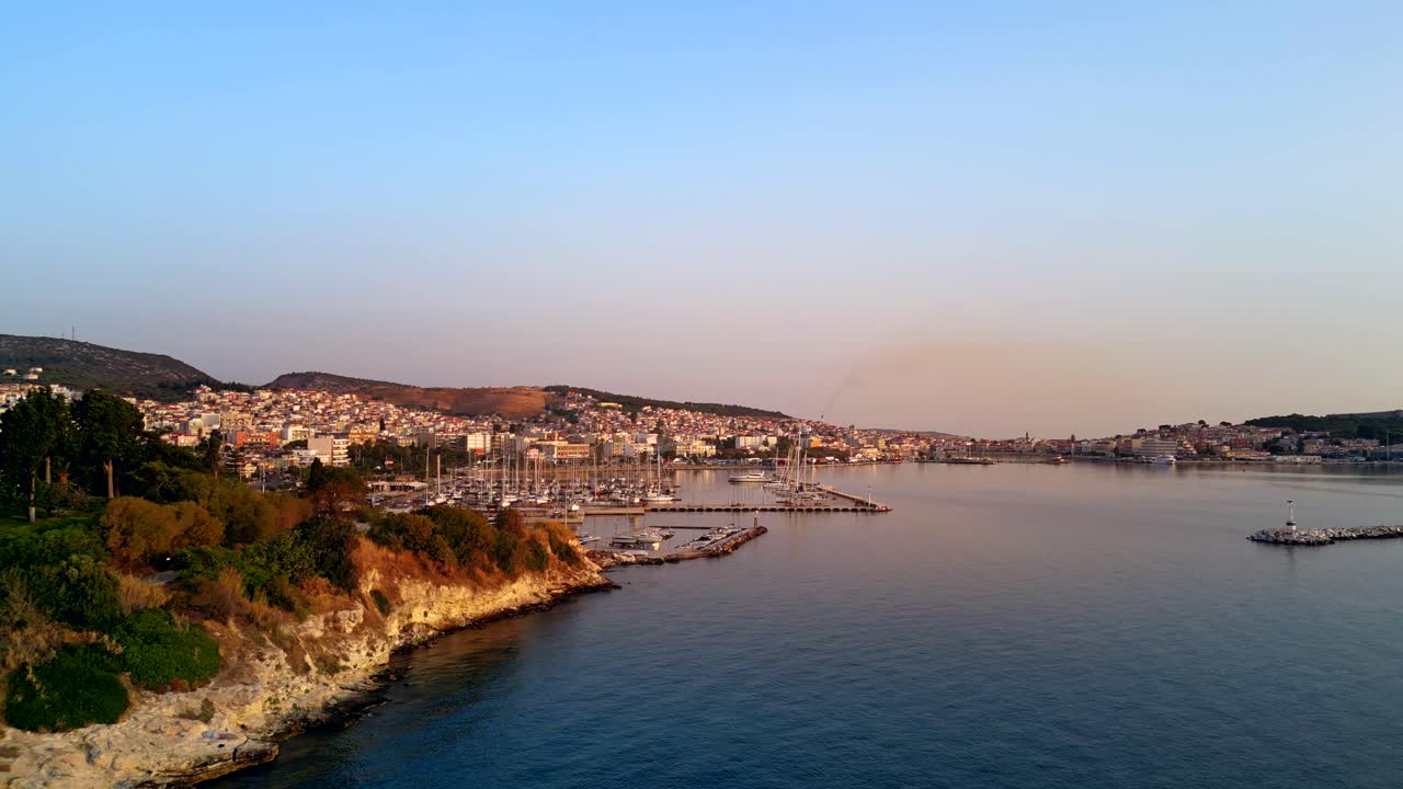 Wide aerial shot of the port of Mytilene, Lesbos, Greece, featuring boats and the glow of orange sunlight.