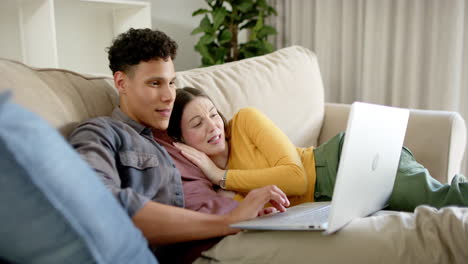 una pareja feliz sentada en el sofá usando una computadora portátil en casa, en cámara lenta