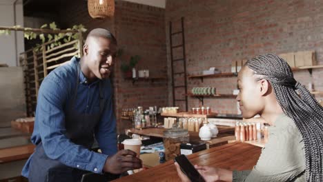 happy african american male barista serving takeaway coffee to female customer, slow motion