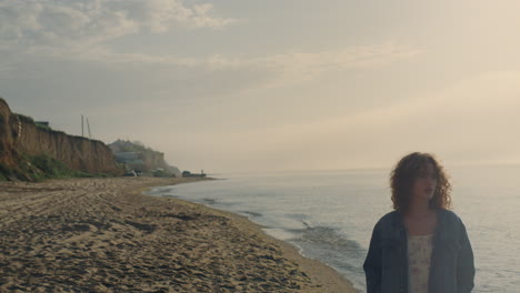 sad woman walking along ocean shore at sunset. depressed girl looking down