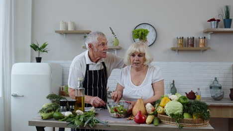 elderly grandparents in kitchen. funny grandpa joking on grandma. putting a lettuce about her head