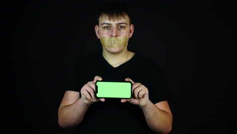 Teenager-Mit-Klebeband-über-Dem-Mund-Hält-Smartphone-Mit-Grünem-Bildschirm