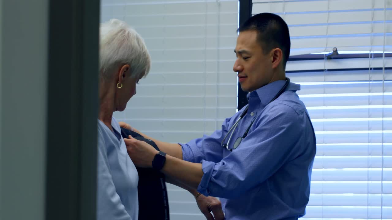 Side view of young Asian male doctor checking blood pressure of senior patient in the clinic 4k