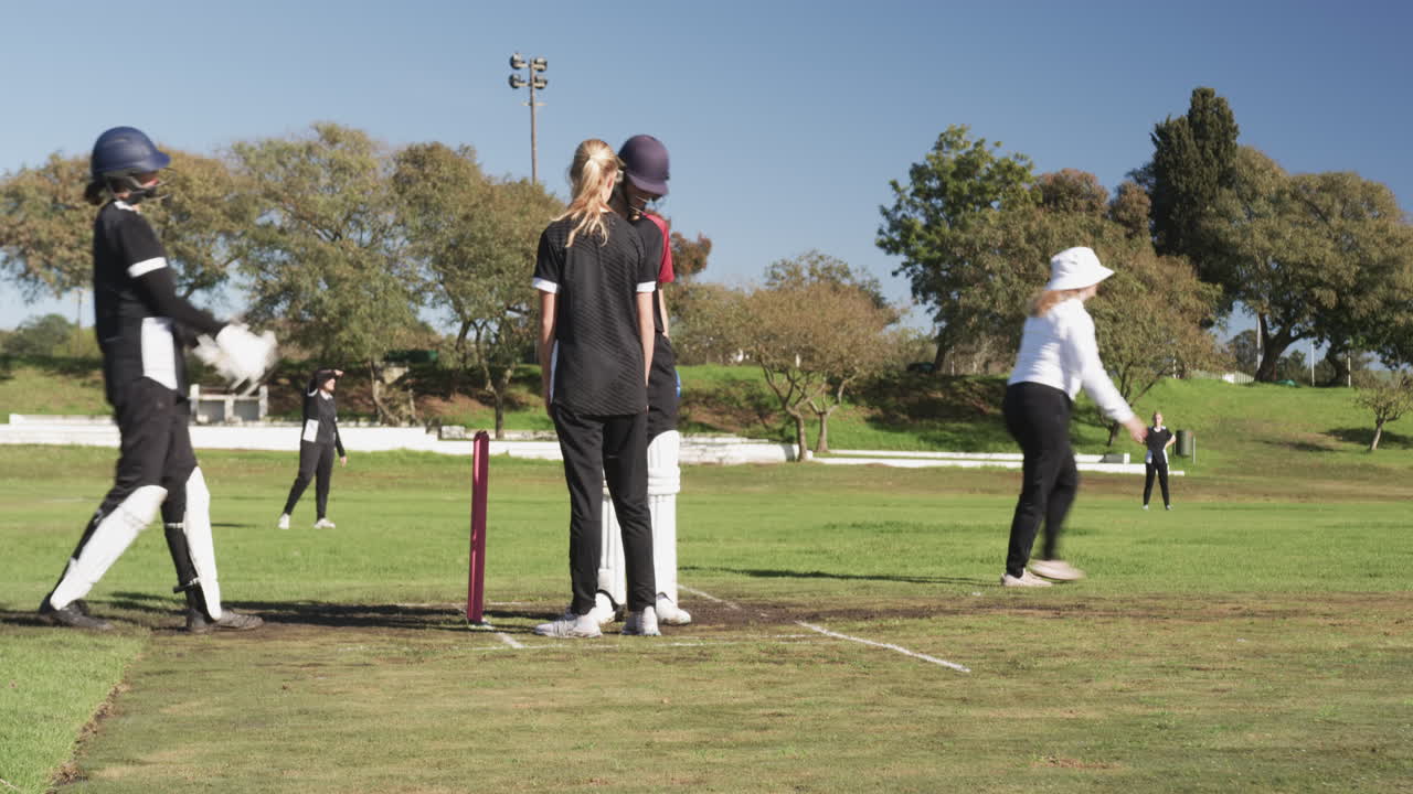 Playing cricket, female players on field during match, wearing protective gear
