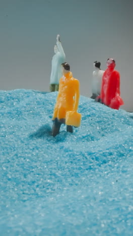 figures of people with bags standing on big sandy hill shimmering at light under grey sky. figurines falling on blue sand shuddering from quakes macro