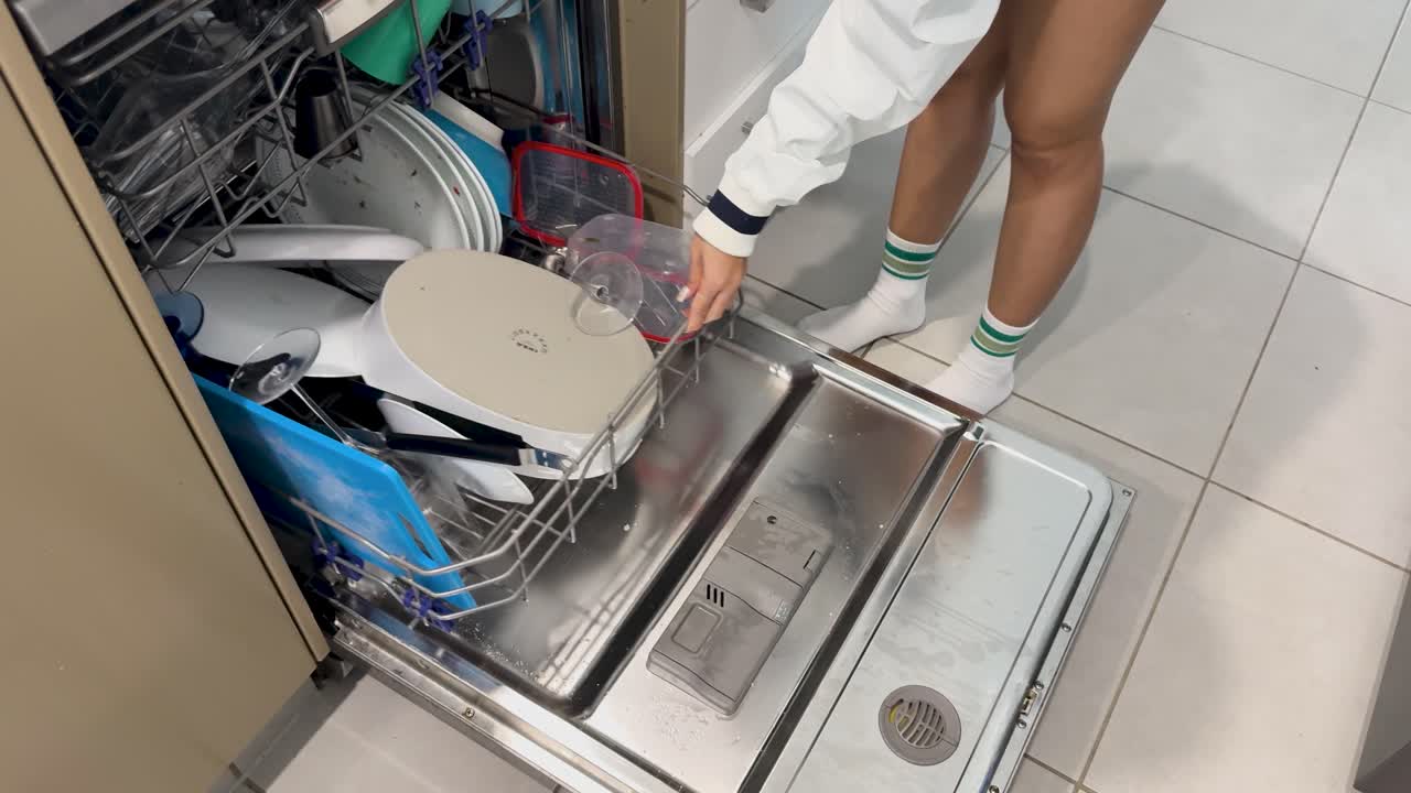 A woman loads dishes into a dishwasher and starts the cycle in a well-lit kitchen