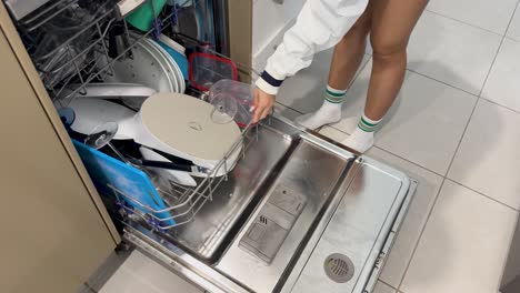 a woman loads dishes into a dishwasher and starts the cycle in a well-lit kitchen