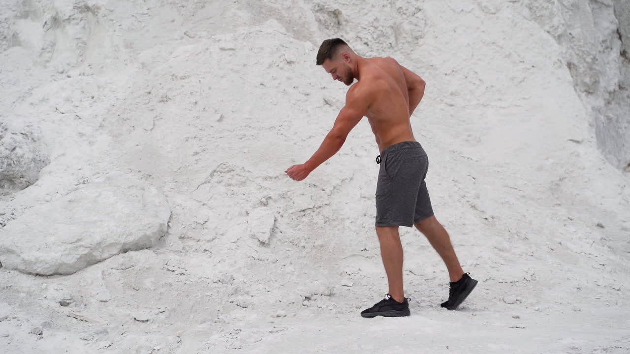Strong athlete posing to camera with his muscular body outdoors. Fitness young man without shirt on the white mountain background.
