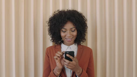 Retrato-De-Una-Joven-Afroamericana-Con-Estilo-Peinado-Afro-Sonriendo-Disfrutando-De-La-Navegación-De-Mensajes-De-Texto-Usando-La-Aplicación-De-Redes-Sociales-Para-Teléfonos-Inteligentes