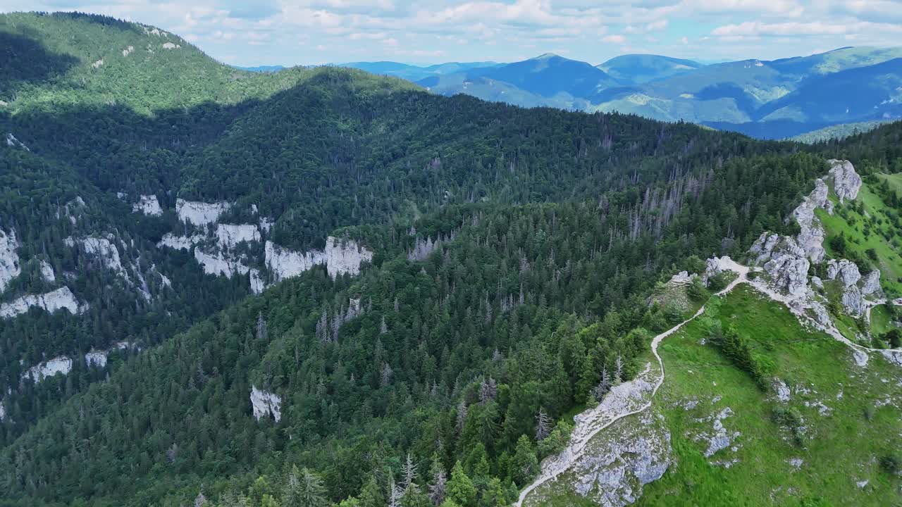 Aerial orbit drone footage captures a rugged rocky ridge surrounded by green alpine slopes and dense forests, highlighting the dramatic landscape and hiking trails. Location: Mala Fatra, Slovakia