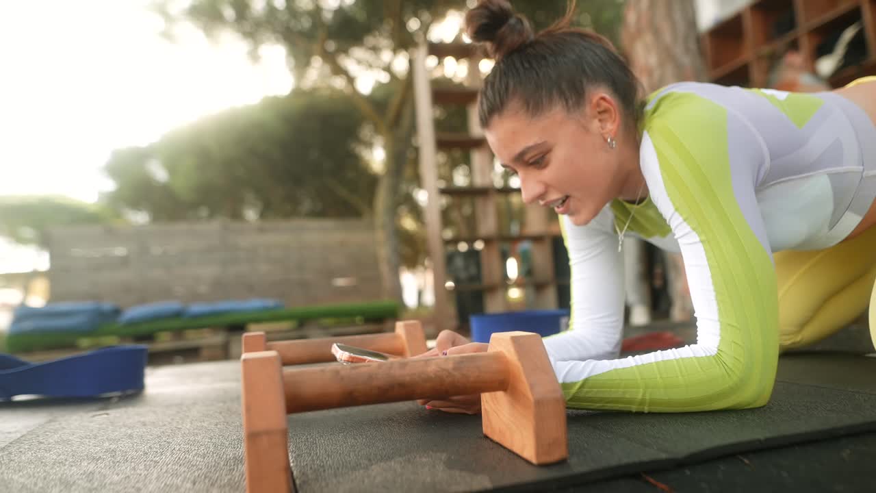 Giovane donna che controlla lo smartphone durante l'allenamento fitness all'aperto