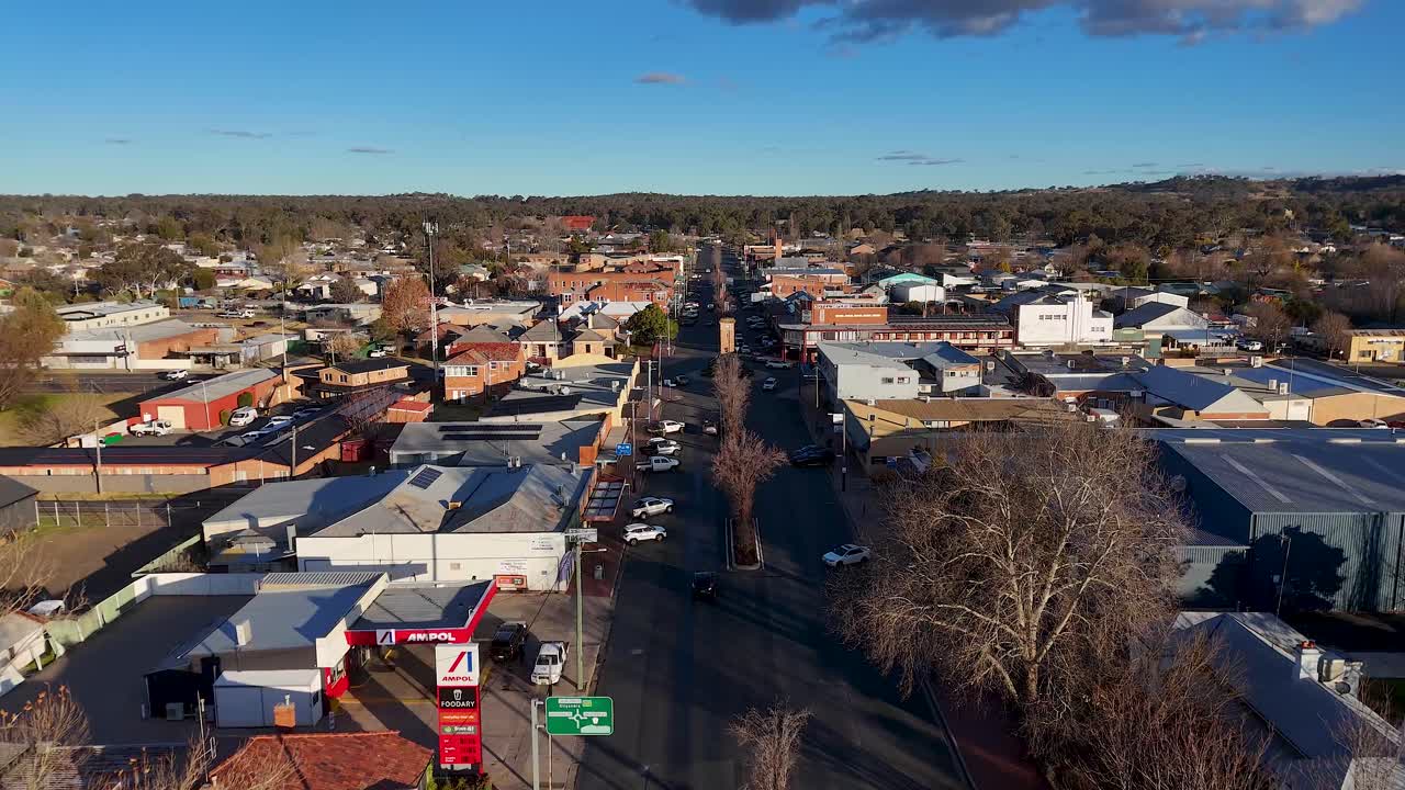 Aerial footage moves steadily above a main street in Coonabarabran, New South Wales, showing urban buildings, sparse traffic, and late afternoon sunlight