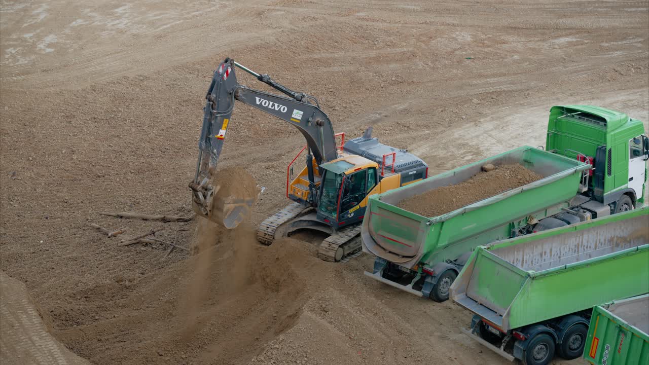 Excavator Digging Dirt and Filling Dump Truck on Active Construction Site for Site Preparation and Building Foundation. Dump Trucks Lined Up to Transport Excavated Dirt to Disposal Location. Sitework