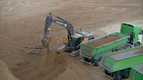 excavator digging dirt and filling dump truck on active construction site for site preparation and building foundation. dump trucks lined up to transport excavated dirt to disposal location. sitework