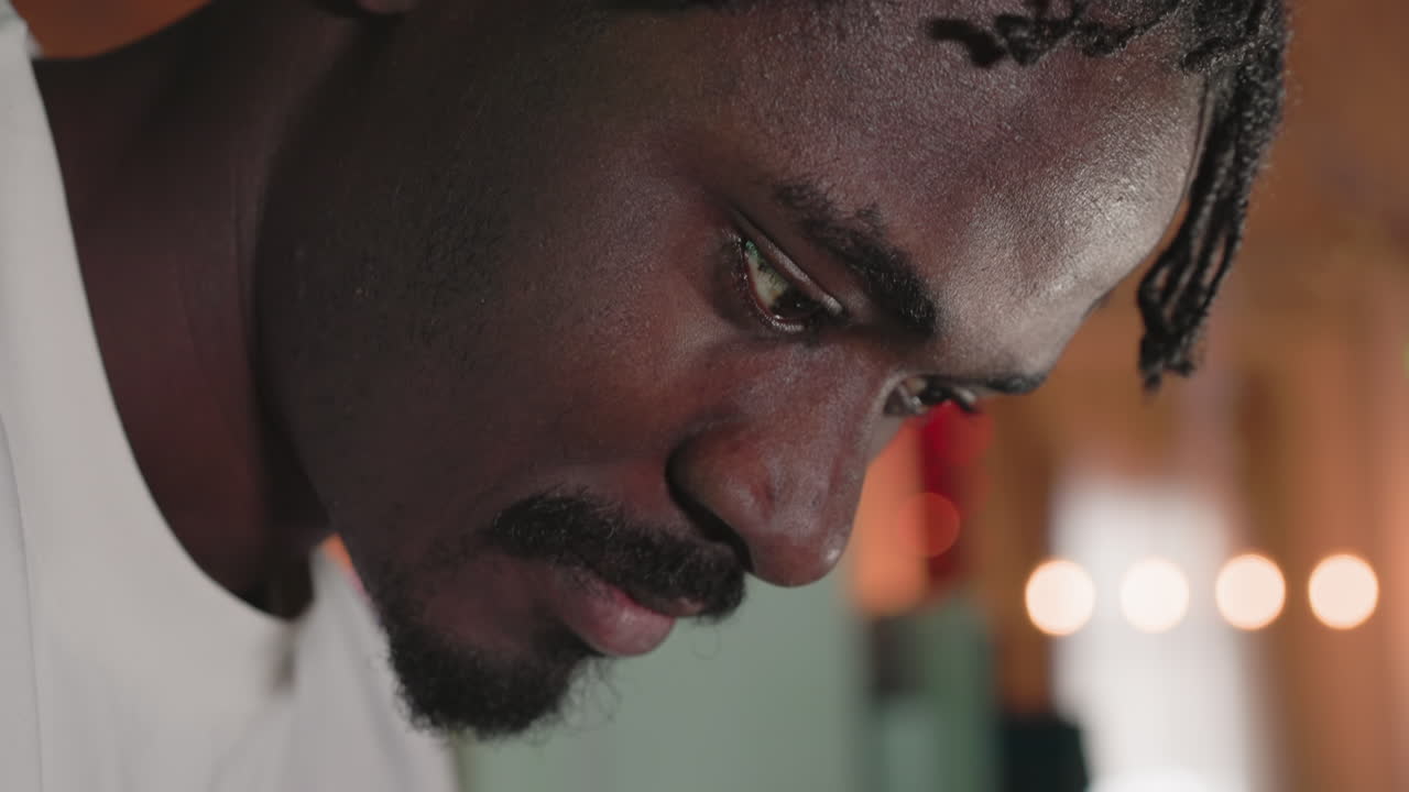 Close-up shot of a man concentrating on a task, with his face in profile. His eyes are focused and his expression suggests deep thought or attention. The background features soft bokeh lighting
