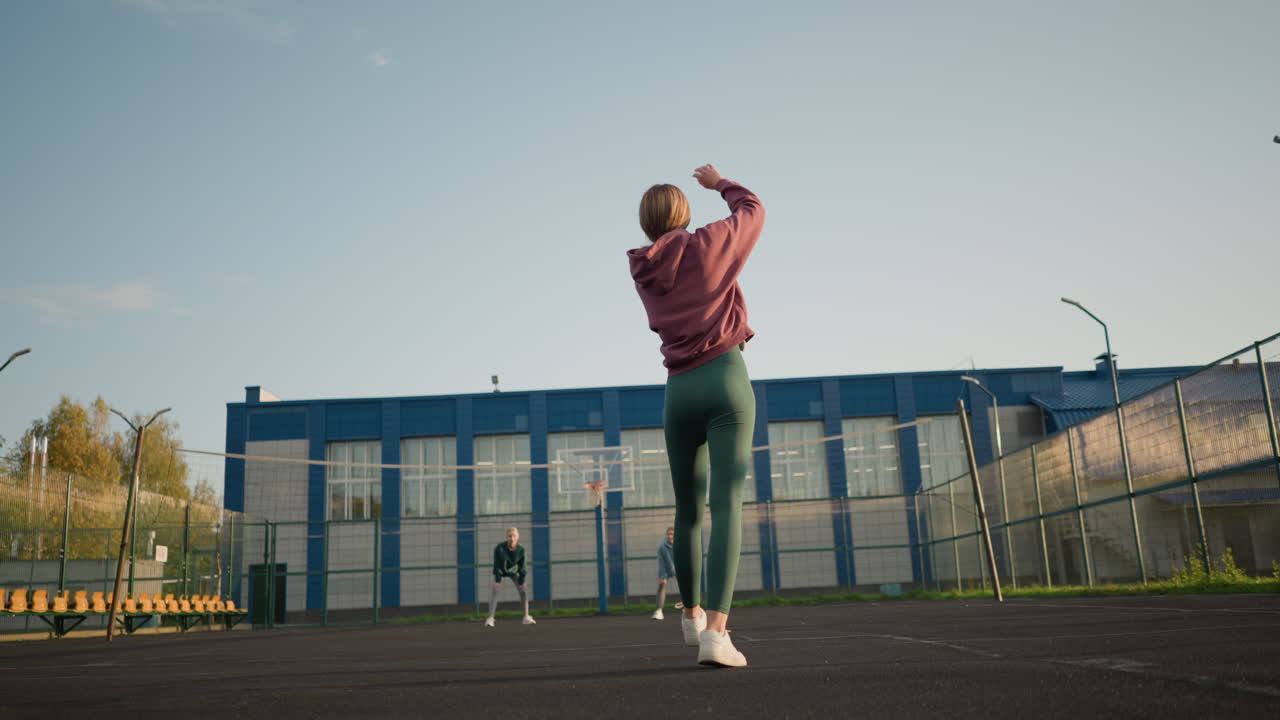 뒷면에는 두 명의 여성이 배경에서 지켜보고 있으며, 건물 뒤에는 공을 잡기 위해 서두르는 파란색의 여자가 있습니다.