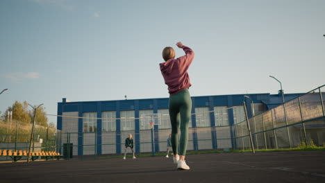 vista trasera de una mujer joven rebotando el voleibol en la cancha con dos mujeres mirando en el fondo, la dama de azul corriendo para atrapar la pelota mientras el edificio es visible detrás de ellos