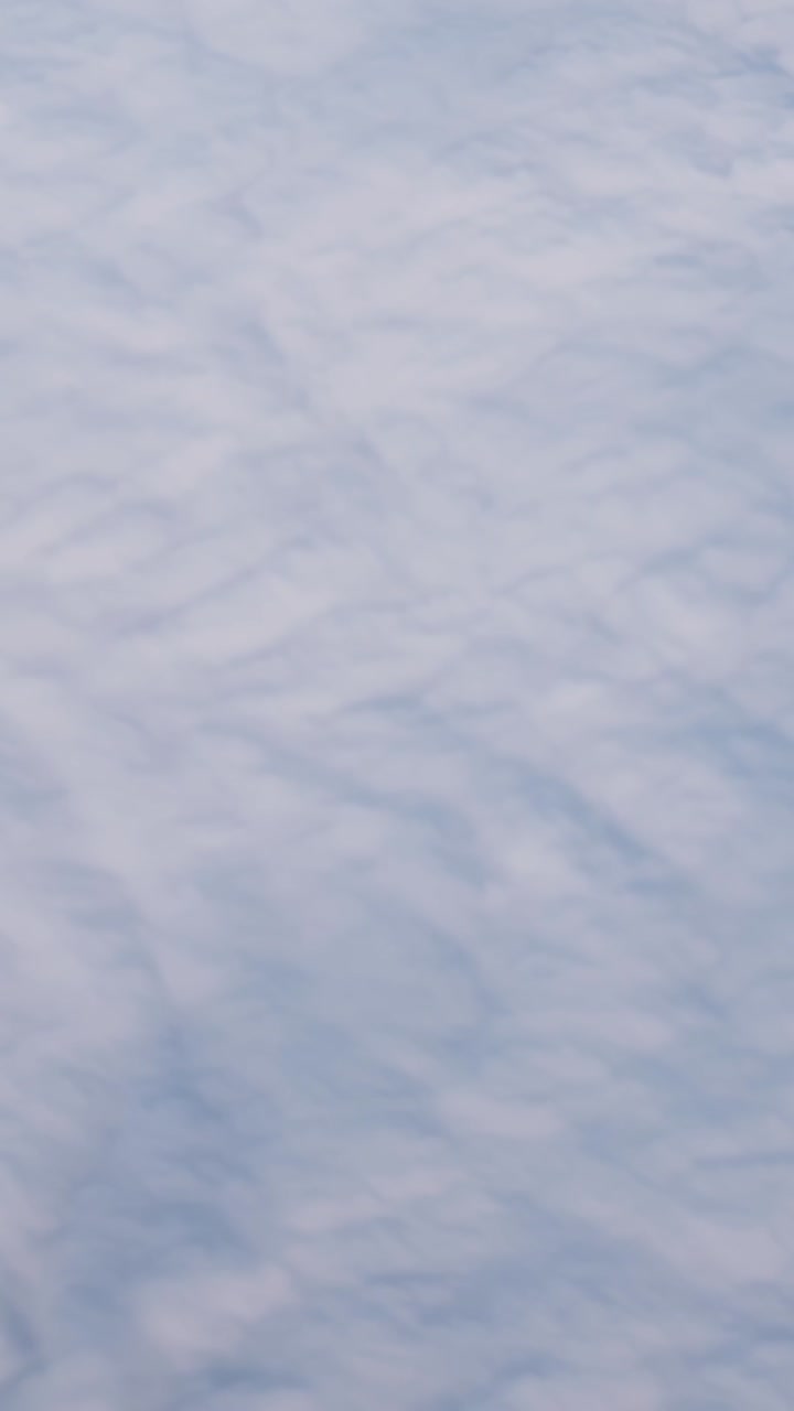 Soft aerial cloud blanket with subtle ripples and pale blue tones, creating a minimalist sky texture background from above during flight