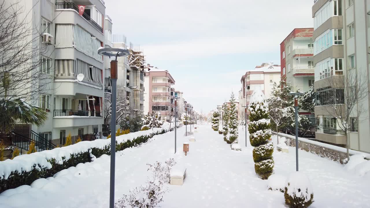 터키 데즈릴리의 구름이 많은 날, 눈으로  ⁇ 인 풍경, 양쪽의 아파트 건물, 그리고 그 사이에 공원을  ⁇ 은 보행자 통로와 같은 낮은 높이의 드론과 같은  ⁇