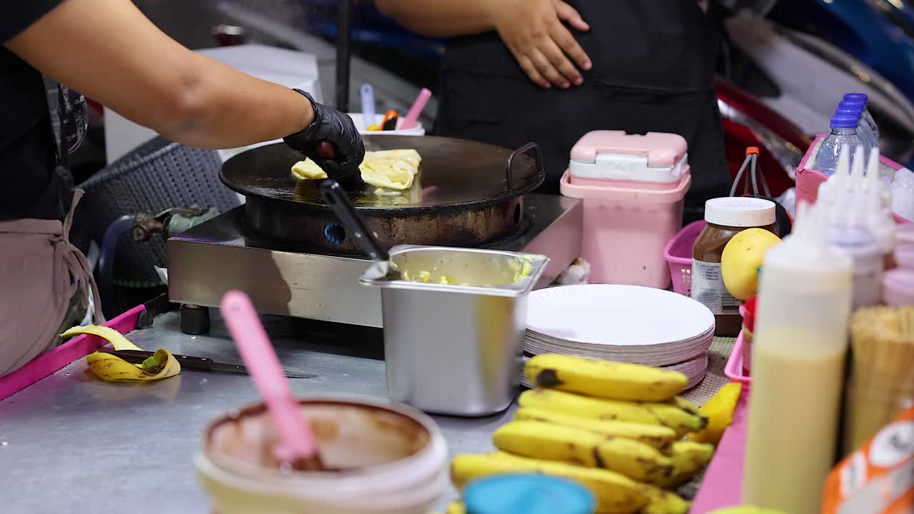 Un venditore ambulante prepara il roti su una vivace strada di Phuket, circondato da ingredienti e colori vivaci, sotto una luce brillante.