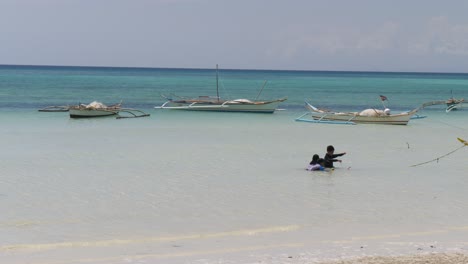 children playing in shallow water on a tropical beach with boats