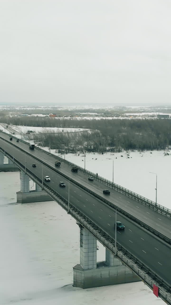 flycam films fast moving transport driving along wide bridge with towers running over cold frozen river close upper view