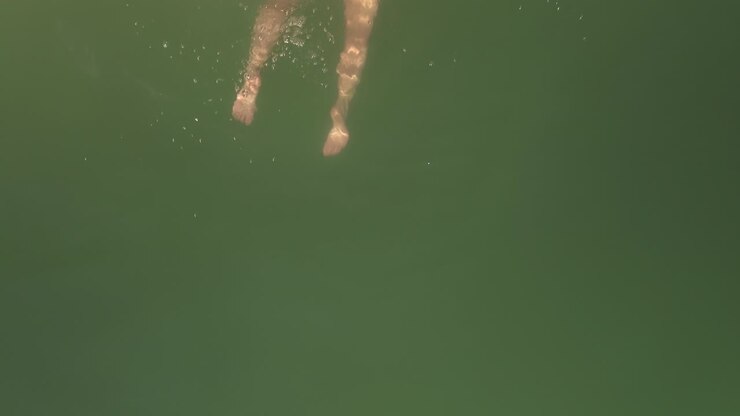 Aerial shot above female in bikini swimwear blowing kiss and swimming in beautiful green water surface